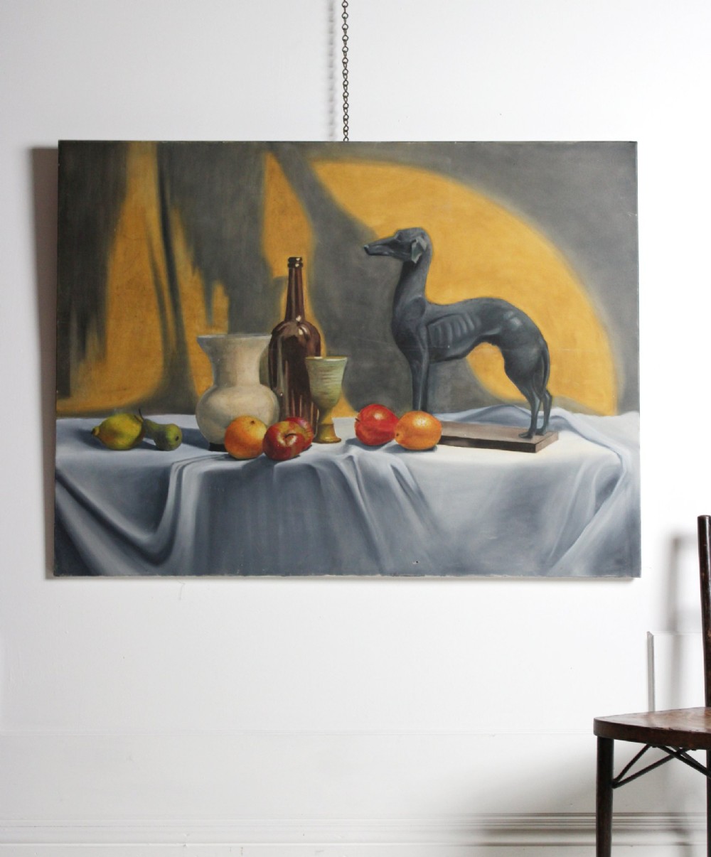 A large mid-20th-century oil painting depicting a draped tabletop still life with fruit, ceramic vessels, and a dark greyhound sculpture against a yellow and grey backdrop. View II