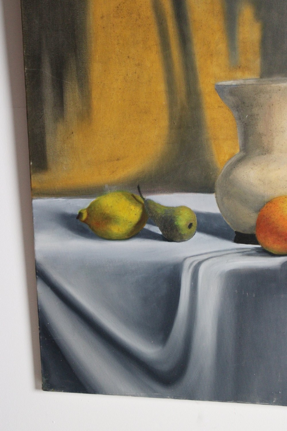 A large mid-20th-century oil painting depicting a draped tabletop still life with fruit, ceramic vessels, and a dark greyhound sculpture against a yellow and grey backdrop. View V