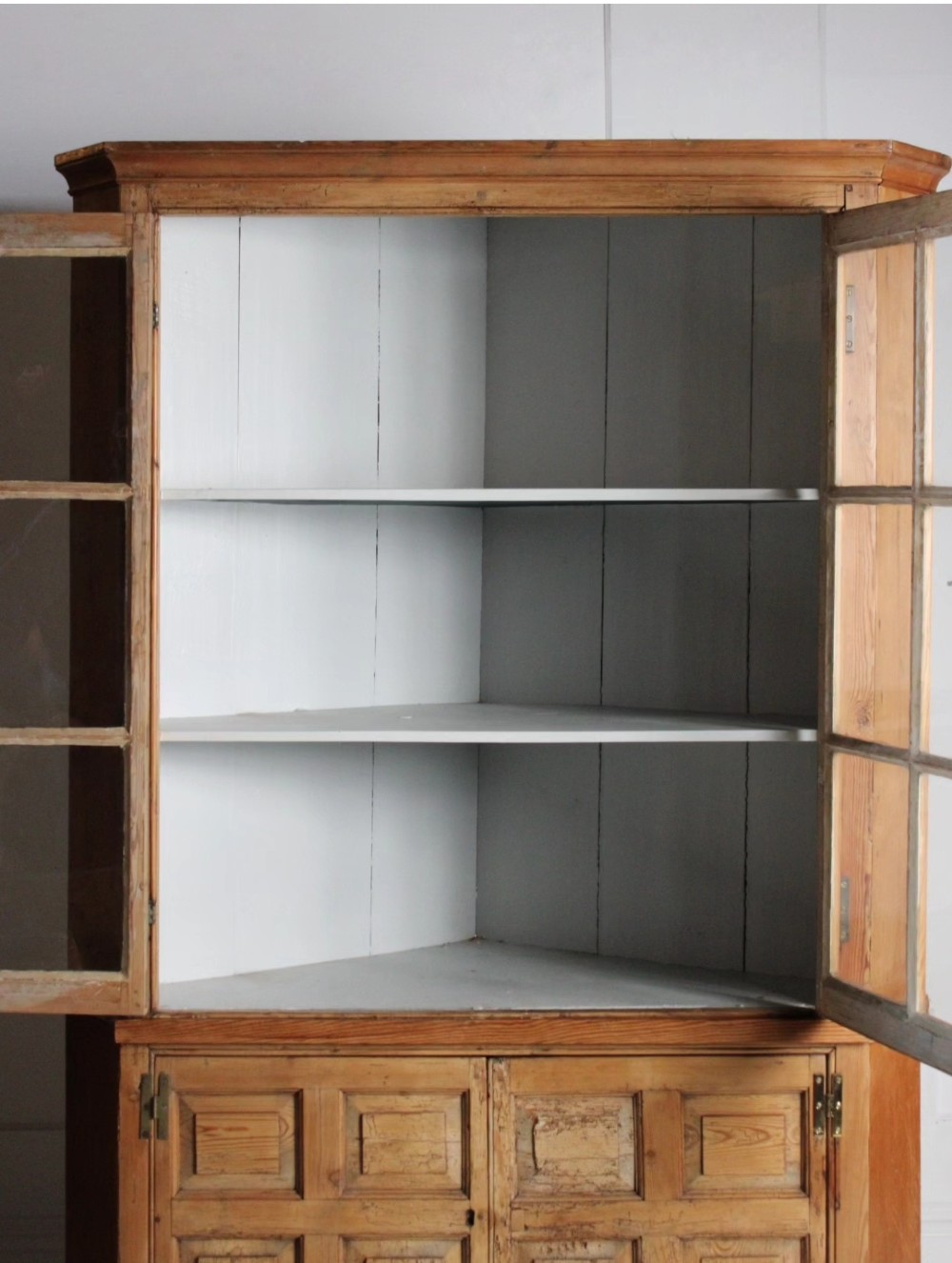 A tall freestanding pine corner cupboard featuring a glazed upper display section with multi-pane glass doors above a two-door lower cabinet with raised timber panels. View III