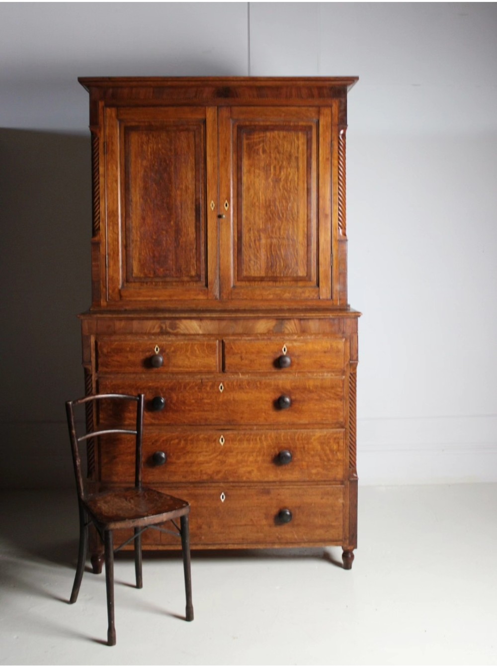 A large Georgian oak housekeepers cupboard featuring an upper two-door cabinet with raised panel doors atop a lower chest of drawers with turned wooden knobs.
