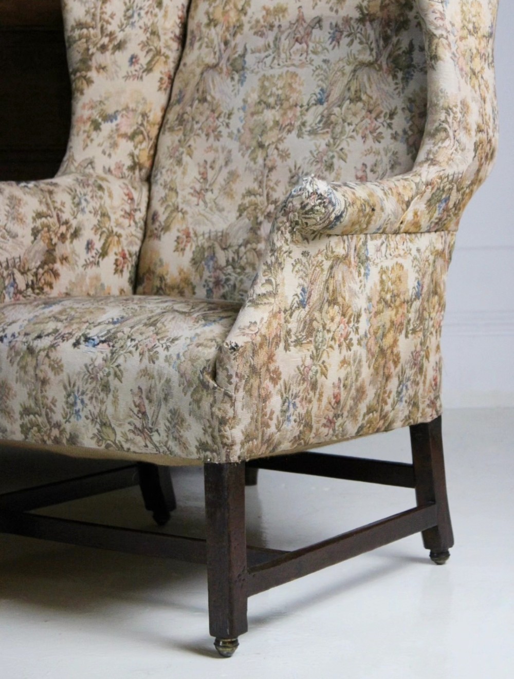 An 18th-century wingback armchair upholstered in patterned tapestry fabric with dark wood legs and brass casters. View II