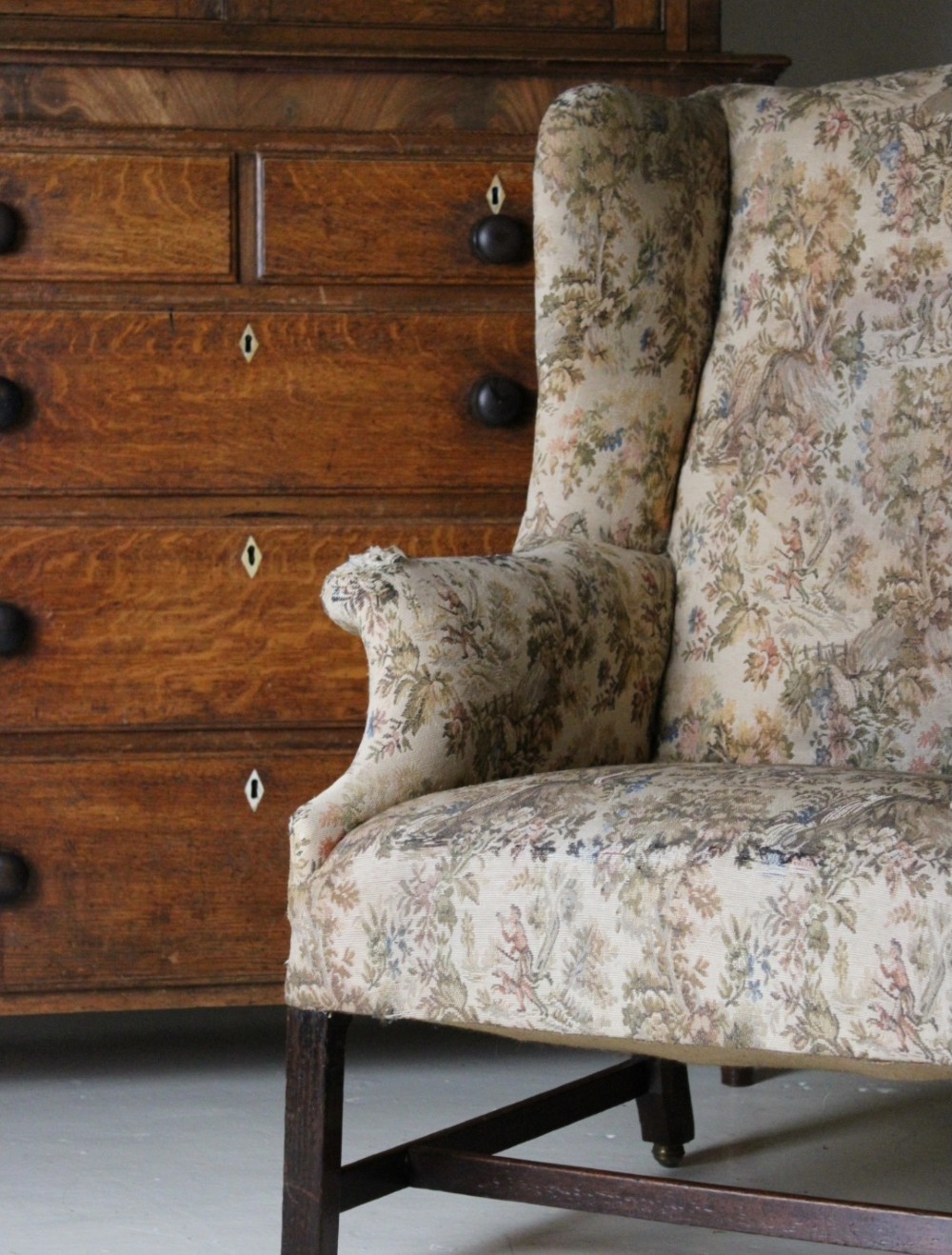 An 18th-century wingback armchair upholstered in patterned tapestry fabric with dark wood legs and brass casters. View III