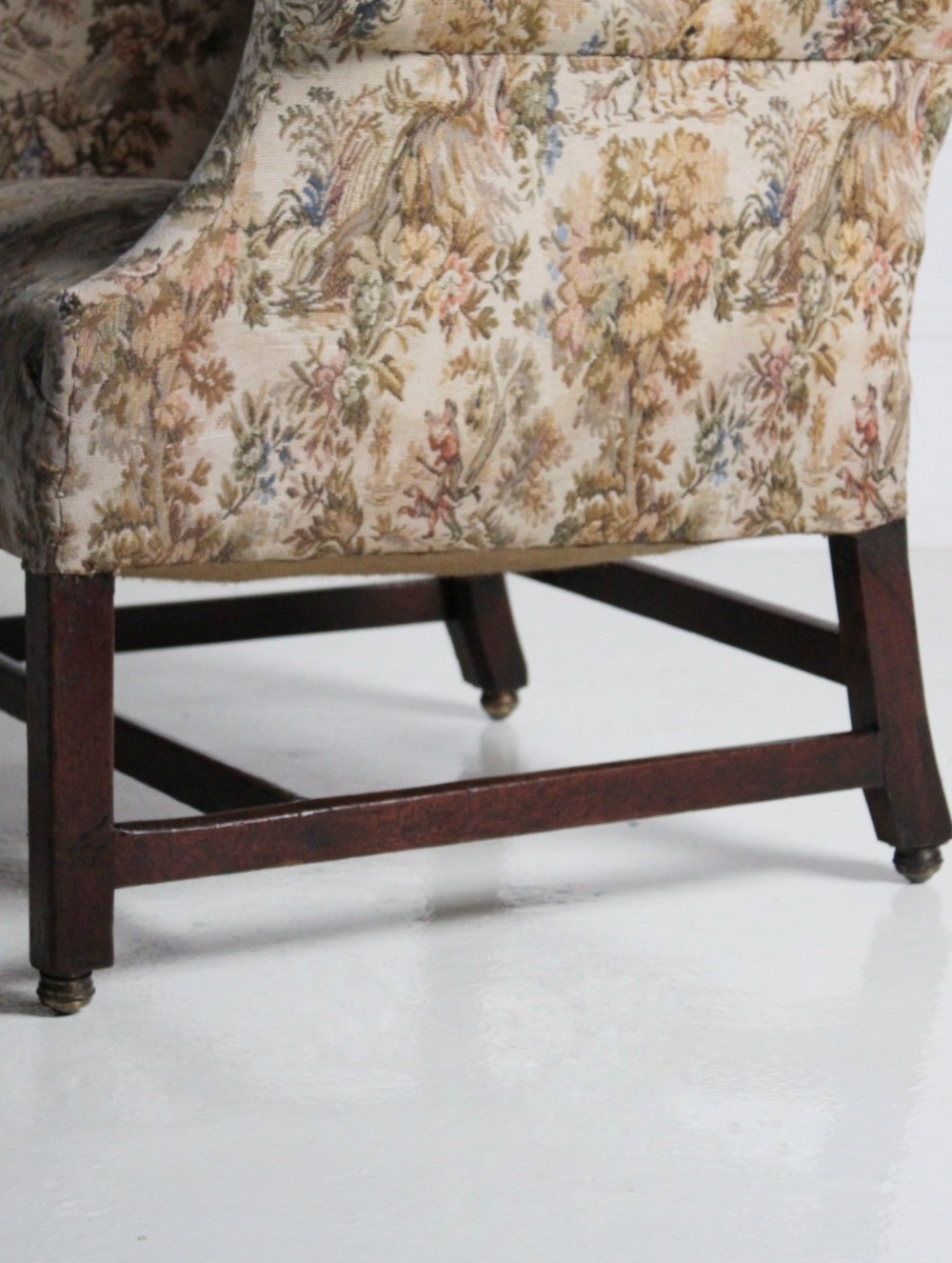 An 18th-century wingback armchair upholstered in patterned tapestry fabric with dark wood legs and brass casters. View IV