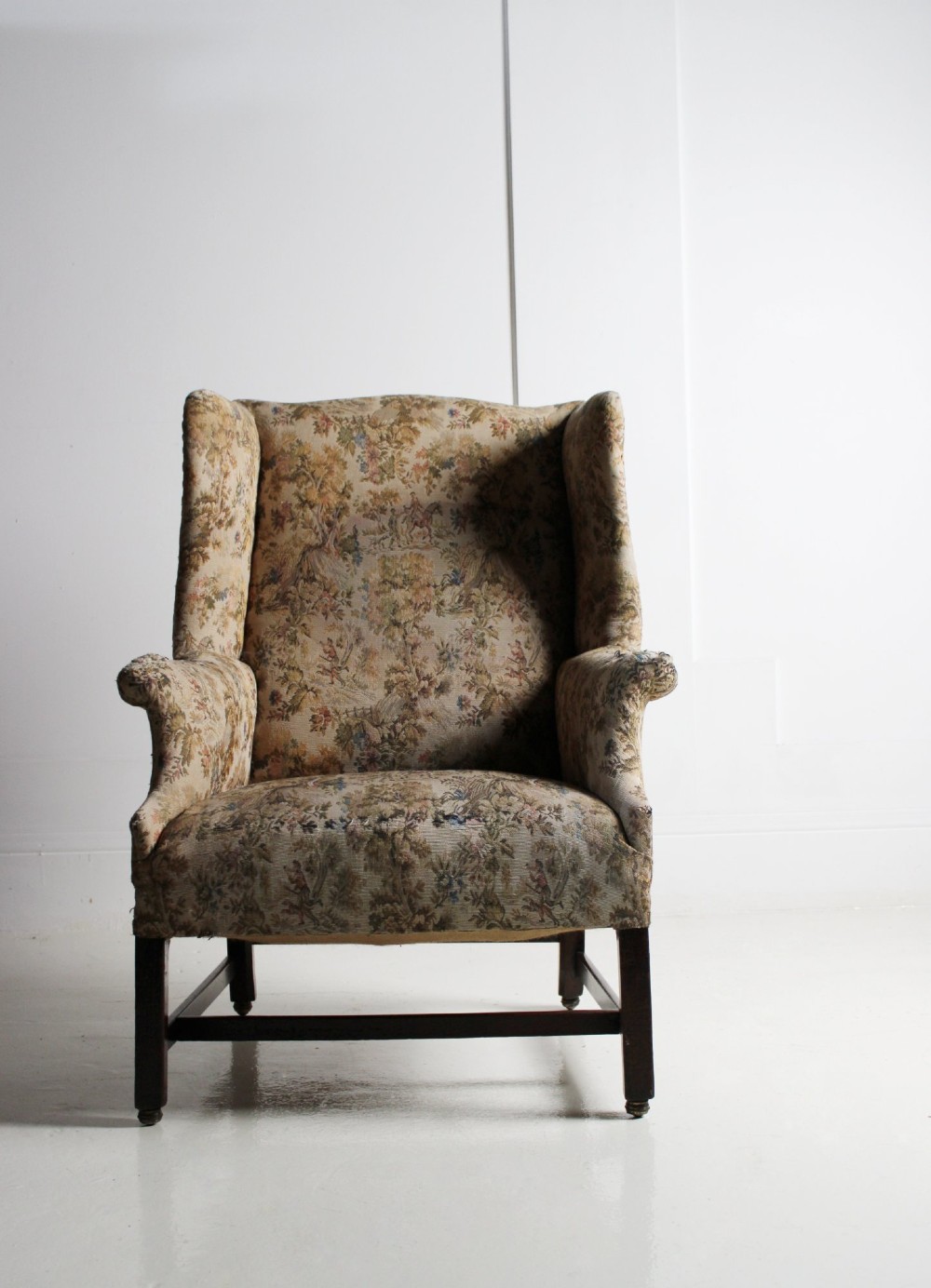 An 18th-century wingback armchair upholstered in patterned tapestry fabric with dark wood legs and brass casters. View V