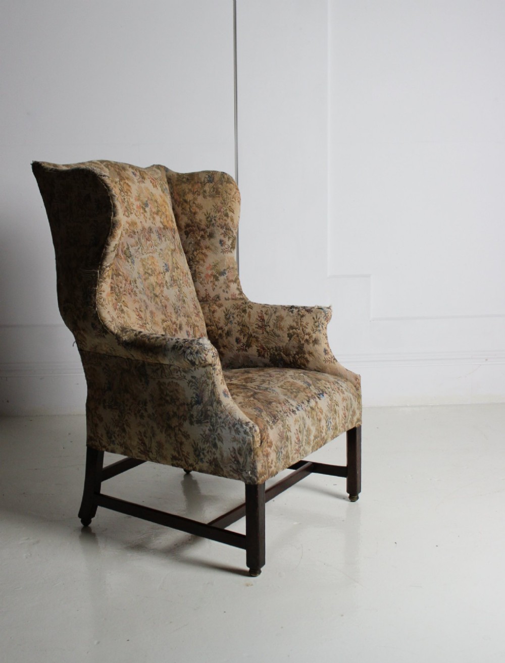 An 18th-century wingback armchair upholstered in patterned tapestry fabric with dark wood legs and brass casters. View VI