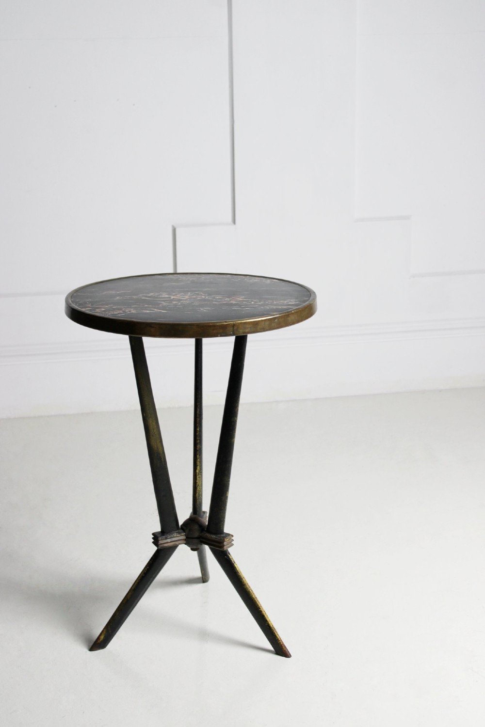 A small round bistro table featuring a dark patterned top surrounded by a brass trim, supported by a black cast iron tripod base.