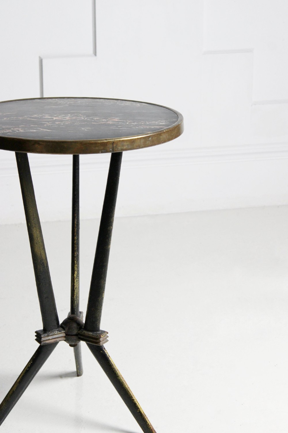 A small round bistro table featuring a dark patterned top surrounded by a brass trim, supported by a black cast iron tripod base. View II