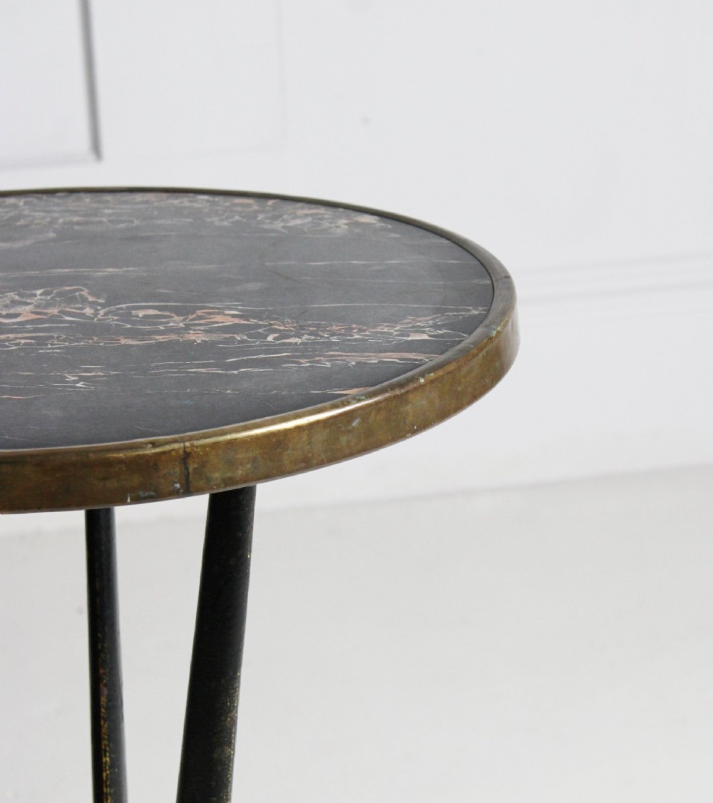 A small round bistro table featuring a dark patterned top surrounded by a brass trim, supported by a black cast iron tripod base. View III