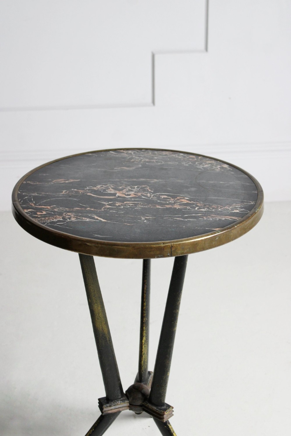 A small round bistro table featuring a dark patterned top surrounded by a brass trim, supported by a black cast iron tripod base. View IV