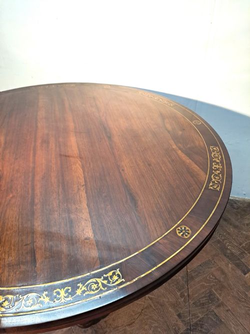 fig 1. A Regency circular rosewood centre table shown tilted vertically, featuring floral brass marquetry inlay along the perimeter and base.