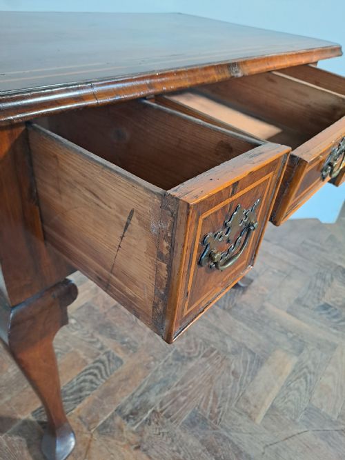 fig 1. An early 18th-century walnut lowboy featuring three crossbanded drawers, brass handles, a shaped apron, and four cabriole legs.