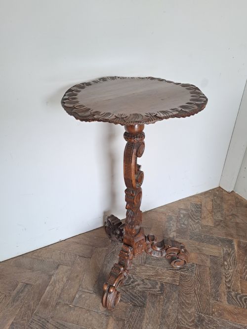 fig 2. A dark brown carved wood tripod table featuring an ornate scalloped rim top, a detailed central pedestal, and three scrolled legs.