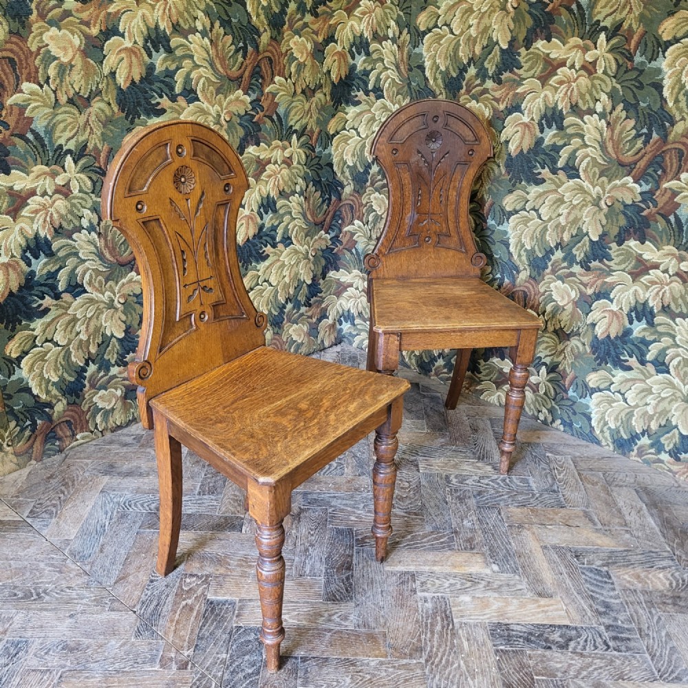 A pair of late Victorian Aesthetic Movement carved oak hall chairs with stylised floral back panels and turned front legs.