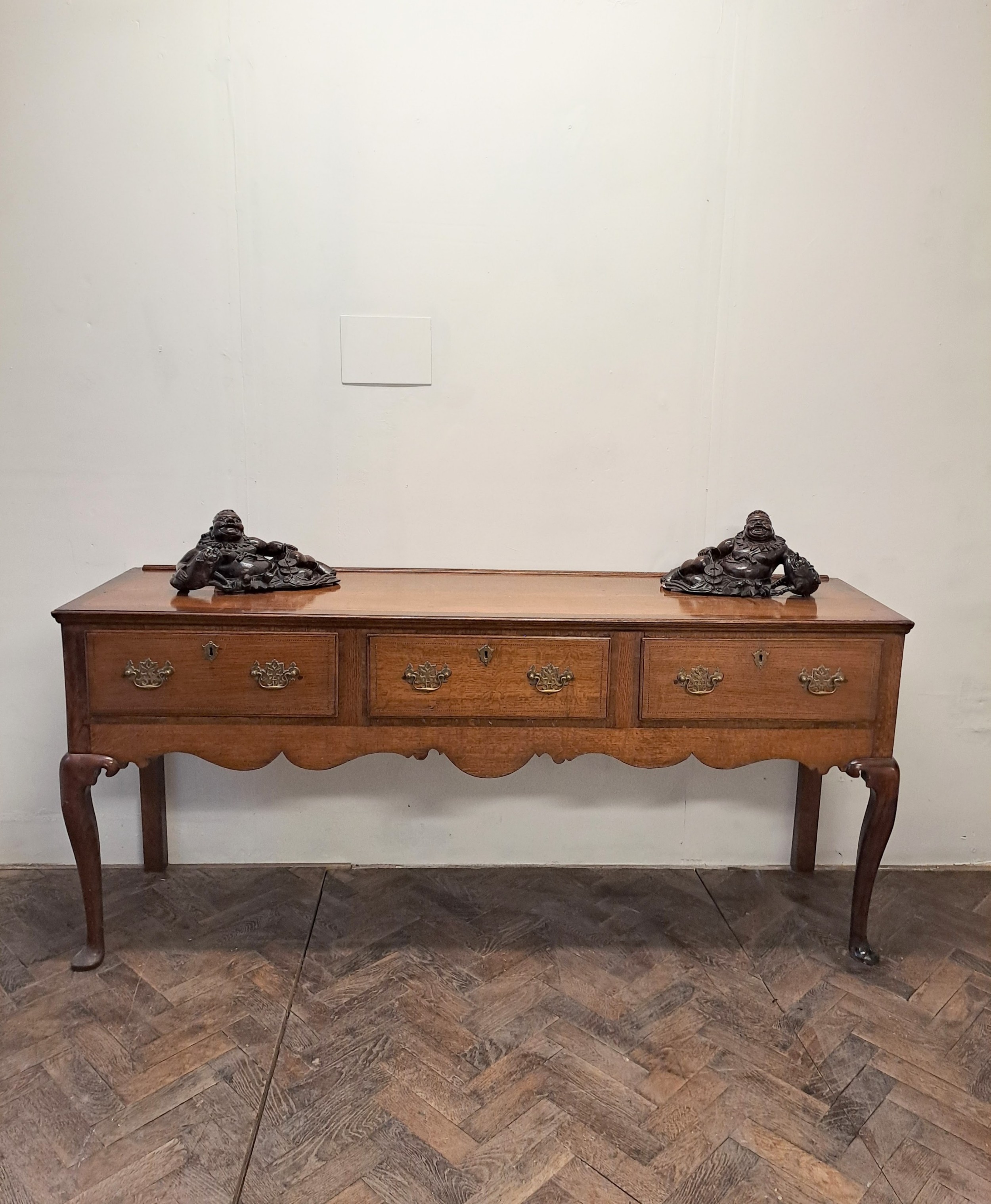 A Georgian oak dresser base featuring three drawers with brass swan-neck handles, a shaped apron, and cabriole legs.