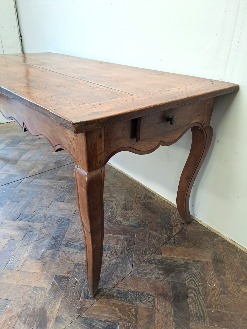 An early 19th-century French farmhouse kitchen table made of warm brown wood with a plank top, scalloped apron, and curved cabriole legs. View VI