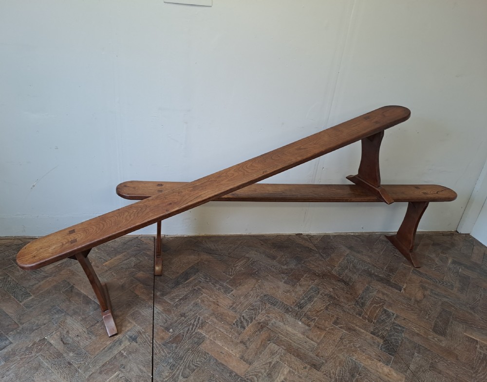 A pair of long, narrow French cherrywood benches with simple plank tops and trestle legs resting on a parquet floor.