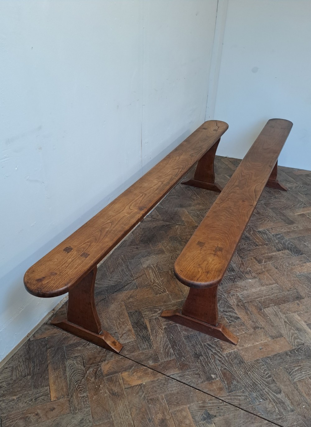 A pair of long, narrow French cherrywood benches with simple plank tops and trestle legs resting on a parquet floor. View V