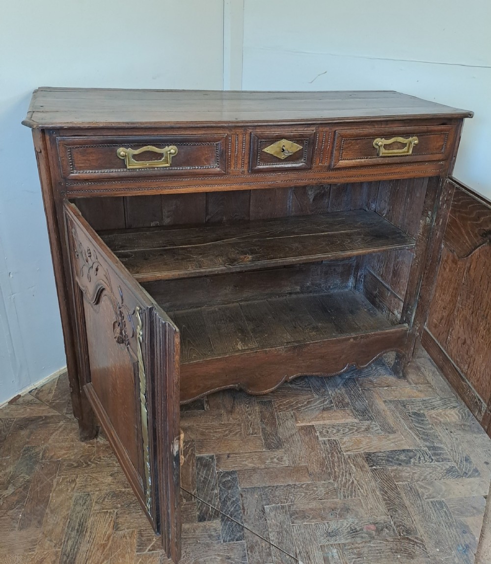 An antique French oak dresser base featuring carved foliate door panels, two top drawers, and decorative brass hardware. View VI