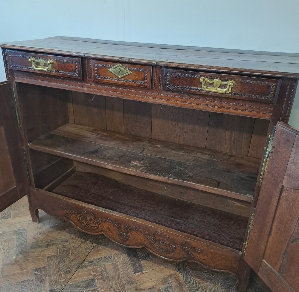 A carved dark oak French provincial buffet base featuring two relief-carved cupboard doors with long brass hinges below two drawers. View VIII