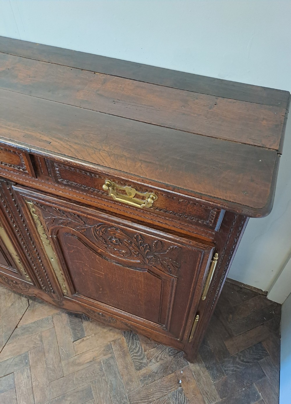 A carved dark oak French provincial buffet base featuring two relief-carved cupboard doors with long brass hinges below two drawers. View VI