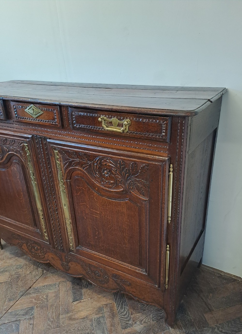 A carved dark oak French provincial buffet base featuring two relief-carved cupboard doors with long brass hinges below two drawers. View VII