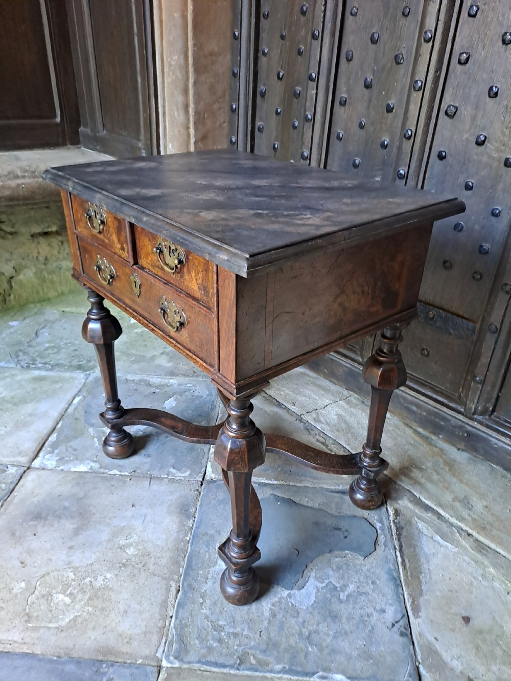 A walnut side table featuring three drawers with brass handles, inverted cup turned legs, and a curved X-stretcher. View III