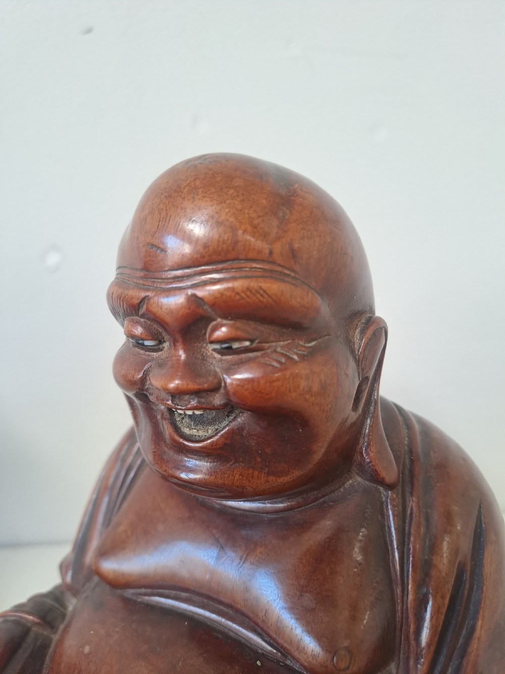 A pair of hand-carved warm brown wooden figures depicting seated, smiling Chinese Laughing Buddhas. View II