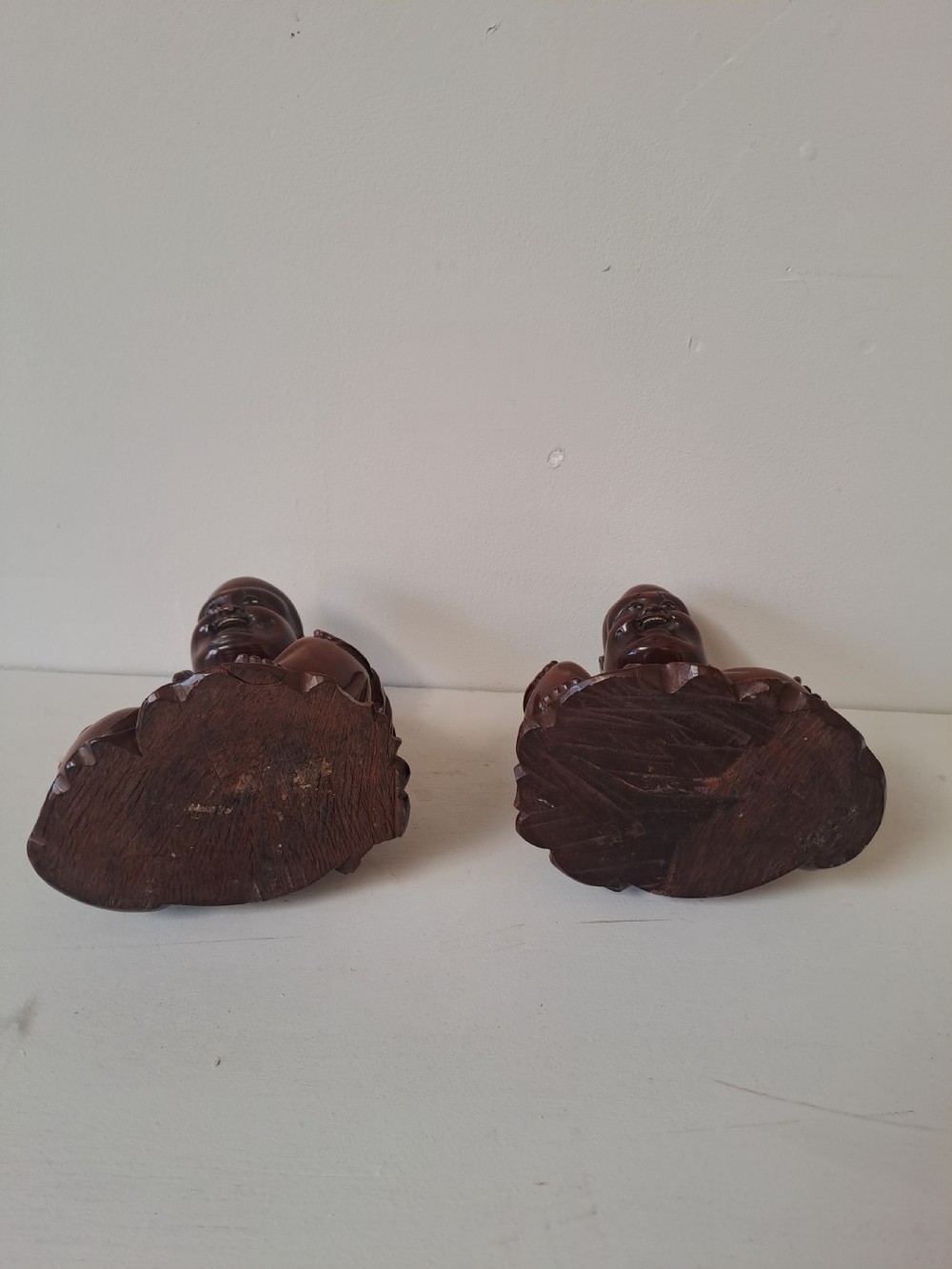 A pair of hand-carved warm brown wooden figures depicting seated, smiling Chinese Laughing Buddhas. View III