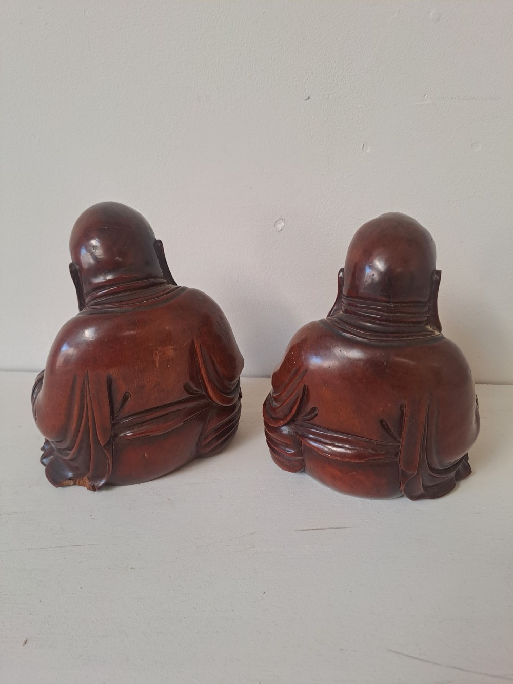 A pair of hand-carved warm brown wooden figures depicting seated, smiling Chinese Laughing Buddhas. View V