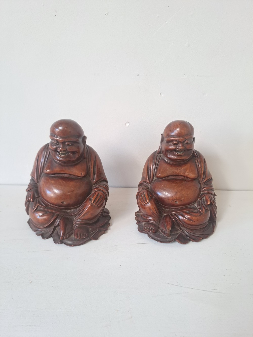 A pair of hand-carved warm brown wooden figures depicting seated, smiling Chinese Laughing Buddhas.