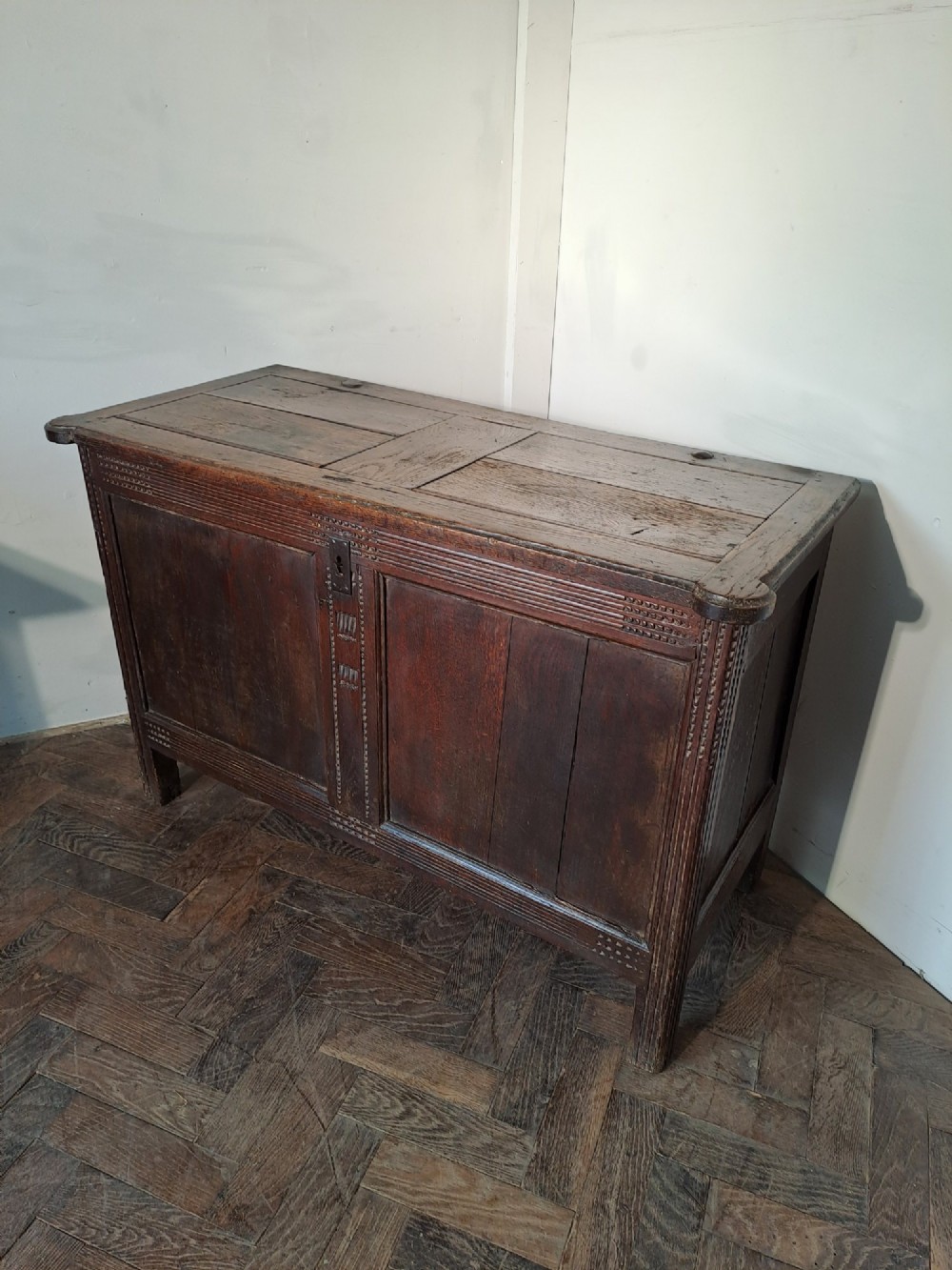 A dark brown French oak coffer featuring panelled sides, carved channel borders, an iron keyhole escutcheon, and a planked timber lid.