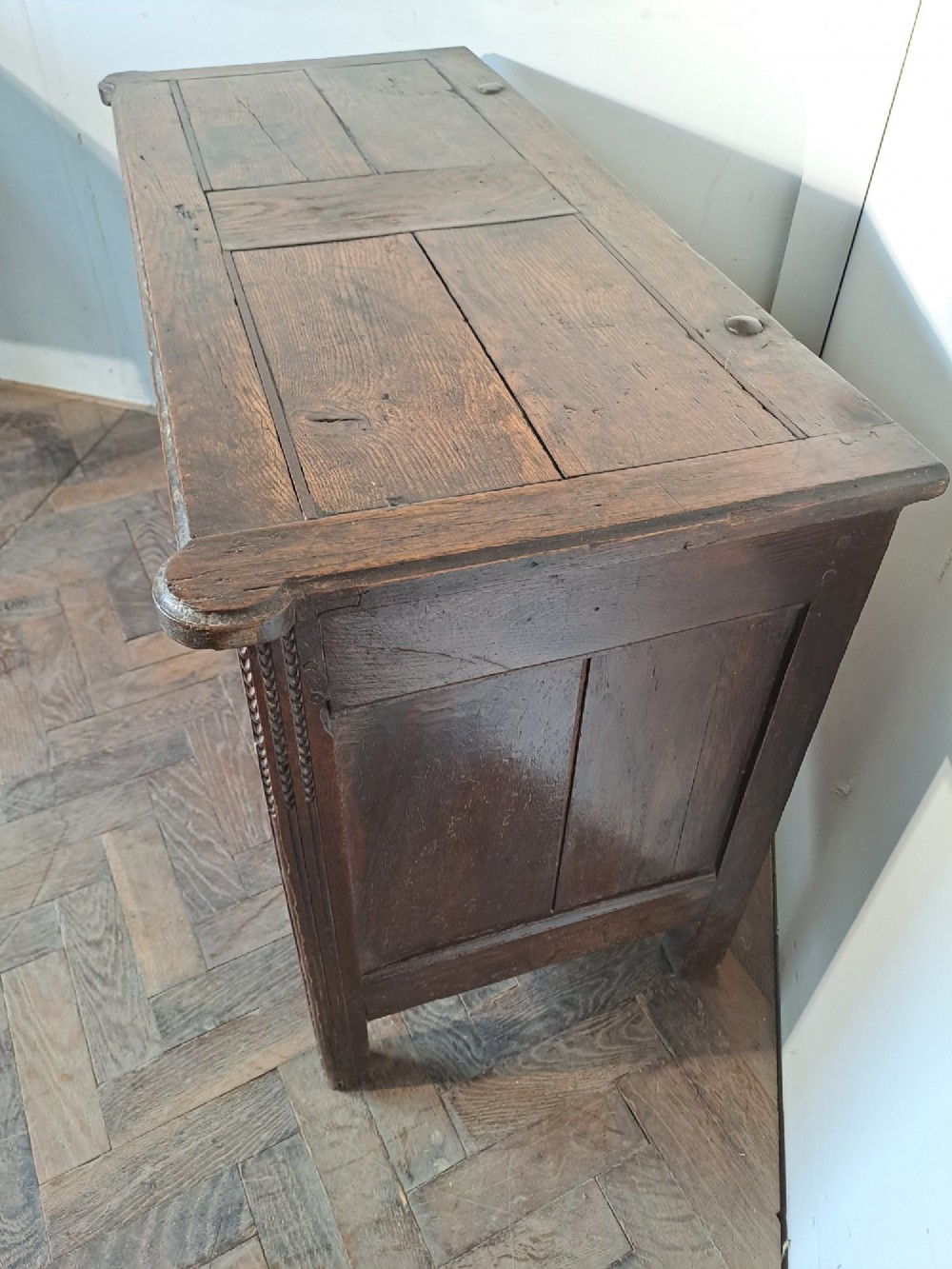 A dark brown French oak coffer featuring panelled sides, carved channel borders, an iron keyhole escutcheon, and a planked timber lid. View II