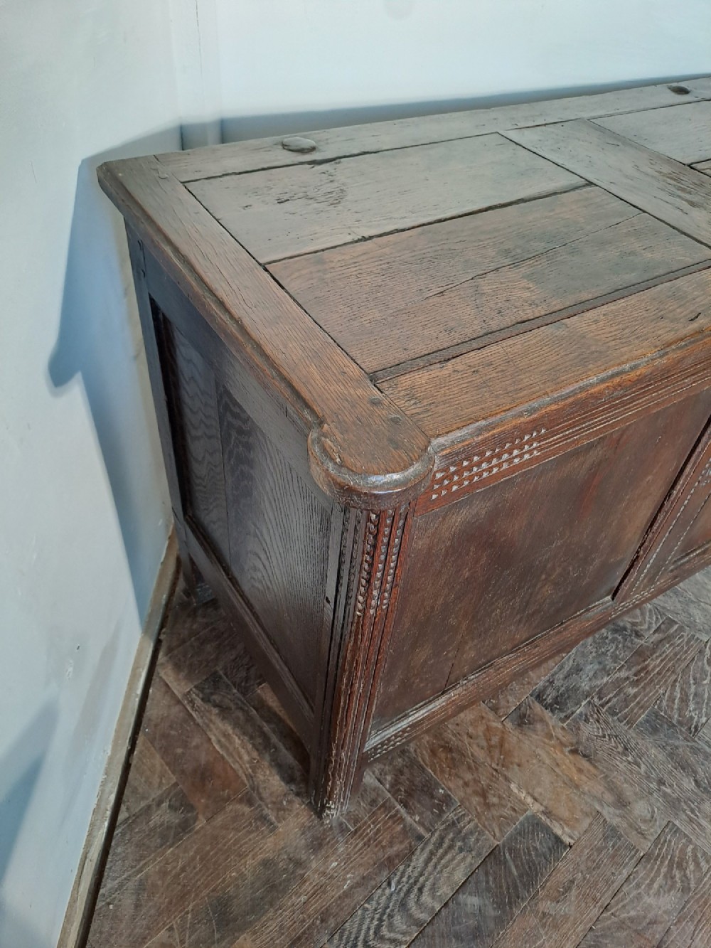A dark brown French oak coffer featuring panelled sides, carved channel borders, an iron keyhole escutcheon, and a planked timber lid. View III