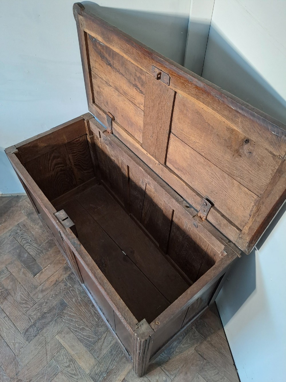 A dark brown French oak coffer featuring panelled sides, carved channel borders, an iron keyhole escutcheon, and a planked timber lid. View IV