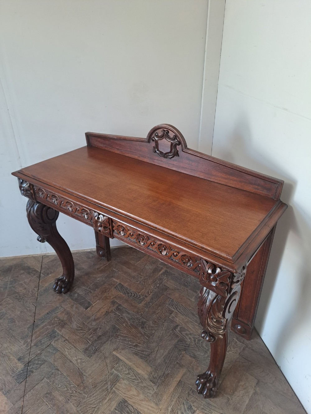 A dark oak console table featuring a carved frieze, front cabriole legs with paw feet, and a low back gallery with a carved shield emblem. View II