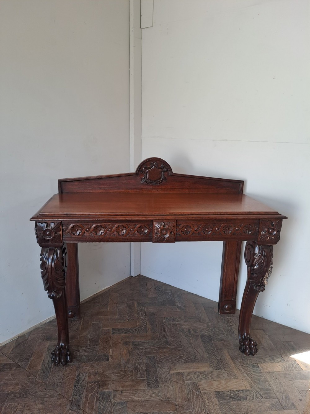 A dark oak console table featuring a carved frieze, front cabriole legs with paw feet, and a low back gallery with a carved shield emblem. View III