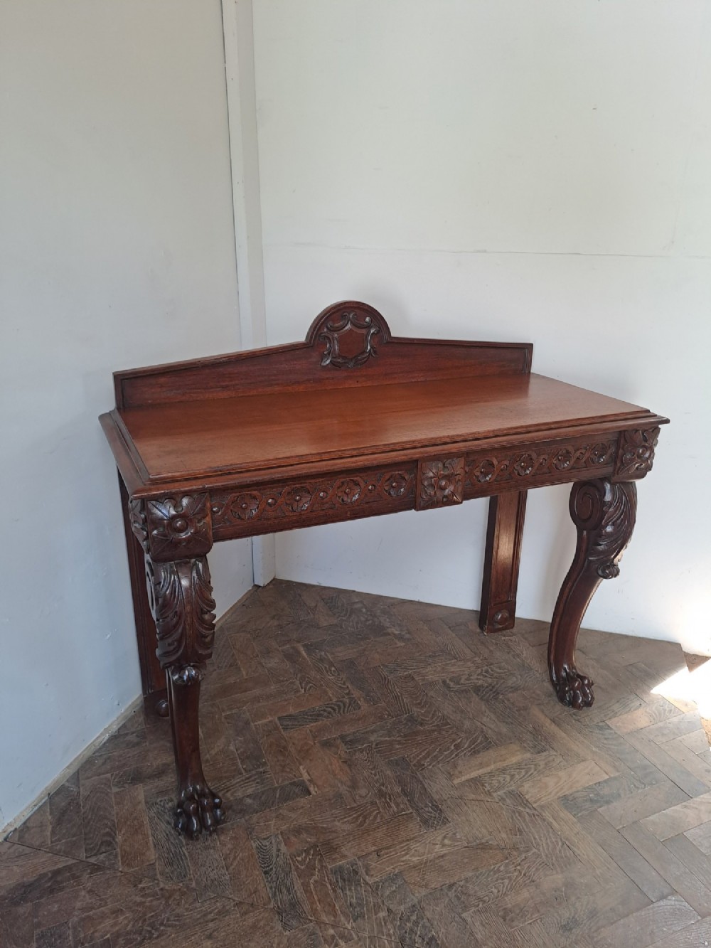 A dark oak console table featuring a carved frieze, front cabriole legs with paw feet, and a low back gallery with a carved shield emblem. View IV