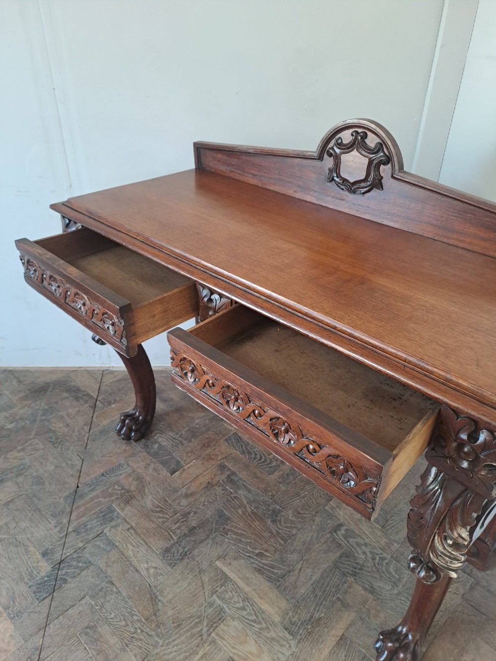 A dark oak console table featuring a carved frieze, front cabriole legs with paw feet, and a low back gallery with a carved shield emblem. View V