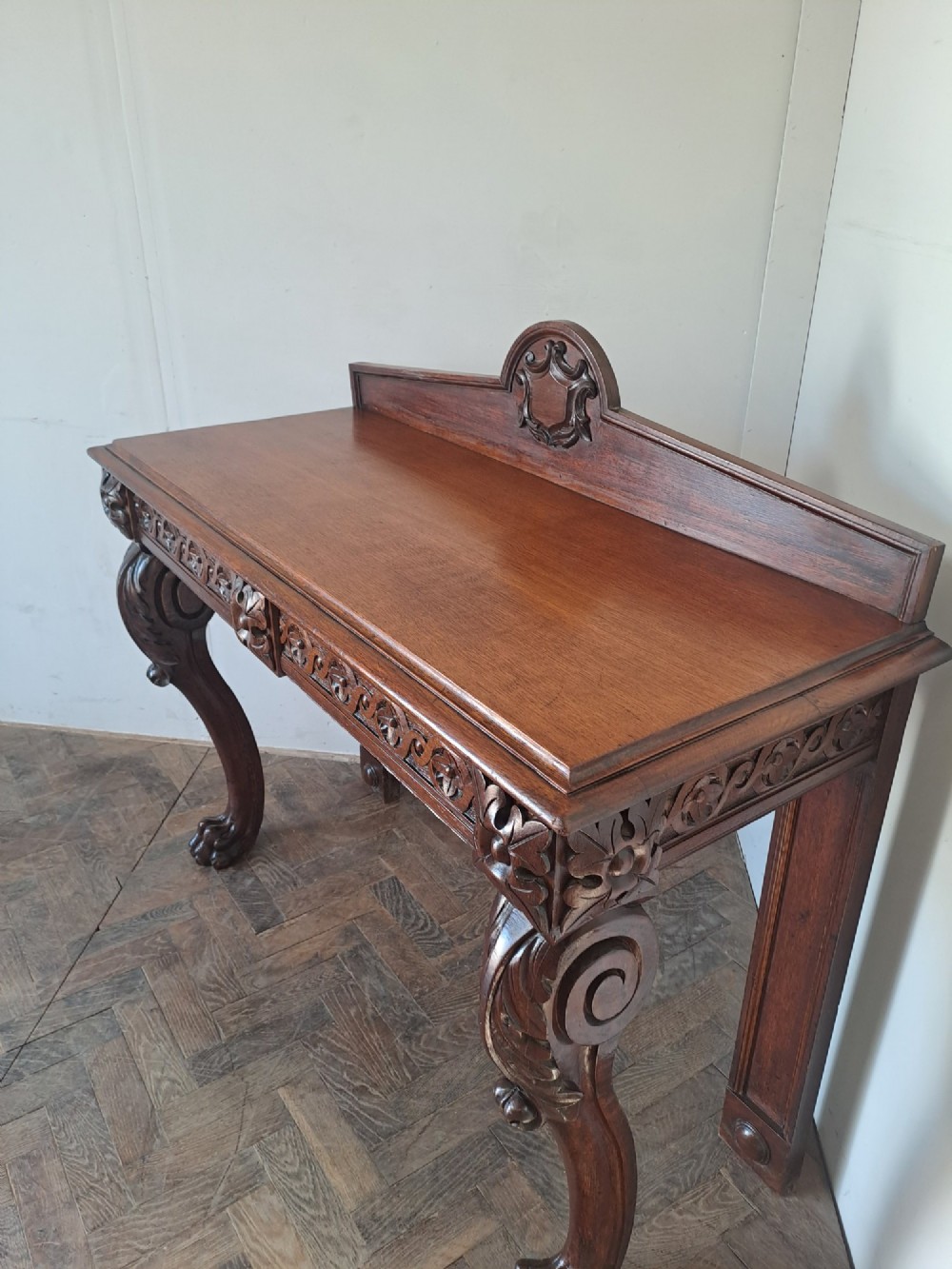 A dark oak console table featuring a carved frieze, front cabriole legs with paw feet, and a low back gallery with a carved shield emblem. View VI