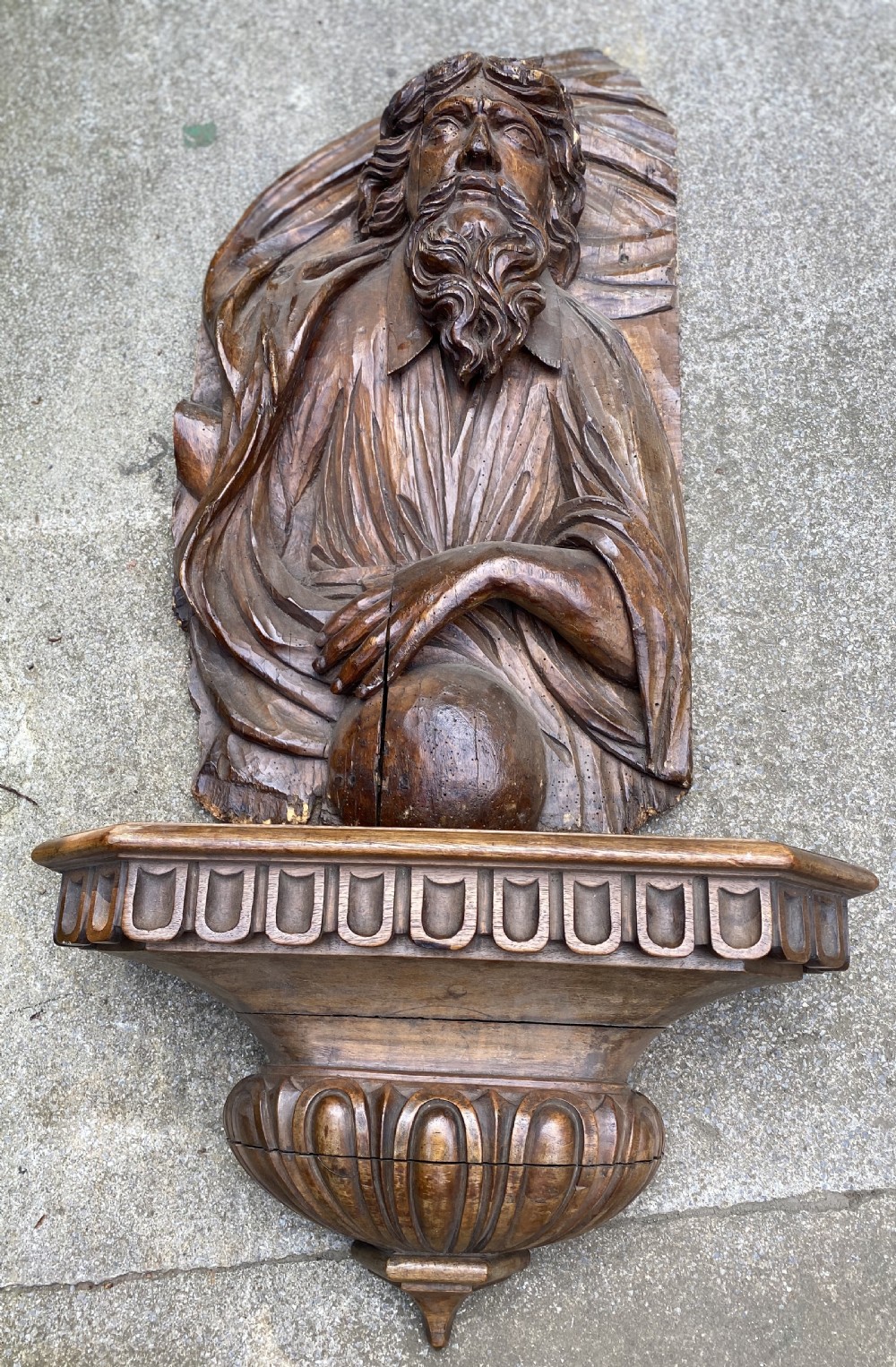A 17th-century carved walnut relief depicting a bearded figure holding an orb, mounted above a decorative carved wooden bracket. View IV