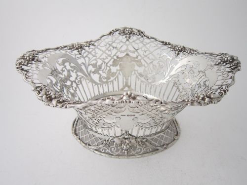 fig 1. An antique George V sterling silver basket featuring intricate pierced lattice metalwork, scrolled grapevine borders, and visible hallmarks.
