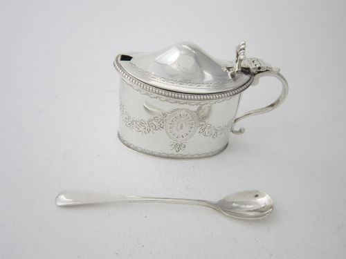 fig 1. An oval sterling silver mustard pot featuring bright-cut engraved patterns, a beaded rim, a scroll handle, and a matching spoon.