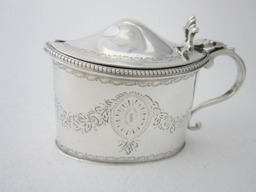 fig 2. An oval sterling silver mustard pot featuring bright-cut engraved patterns, a beaded rim, a scroll handle, and a matching spoon.