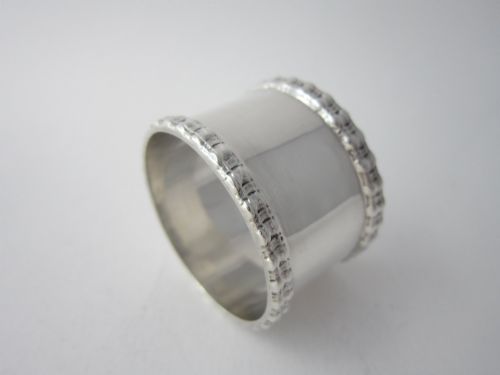 fig 1. An Edwardian sterling silver napkin ring featuring embossed patterned borders along the top and bottom rims.