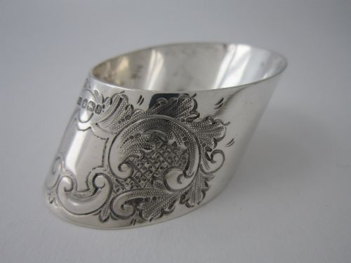 fig 1. A Victorian sterling silver napkin ring featuring intricate foliate scroll engraving and visible British hallmarks on a reflective curved surface.