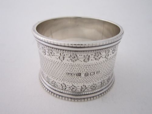 fig 1. An antique sterling silver napkin ring featuring intricate bright-cut floral engraving, engine-turned lattice patterning, a central cartouche, and beaded borders.