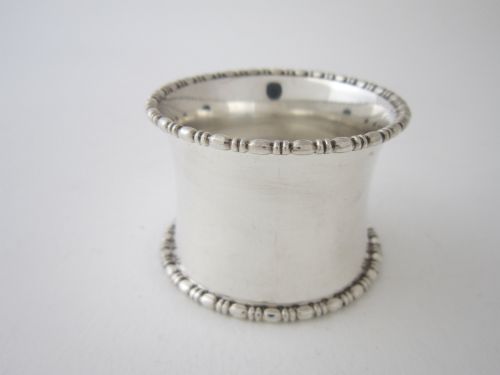 fig 1. A cylindrical George V sterling silver napkin ring featuring decorative beaded rims along both edges and stamped British hallmarks on the outer surface.