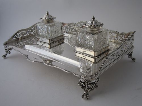 fig 2. A George V sterling silver tray featuring a pierced gallery, scroll feet, a central pen recess, and two square cut-glass inkwells with silver lids.