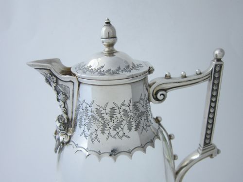 fig 1. A Victorian clear glass claret jug with an engraved sterling silver collar, hinged lid with finial, and an ornate scroll handle.