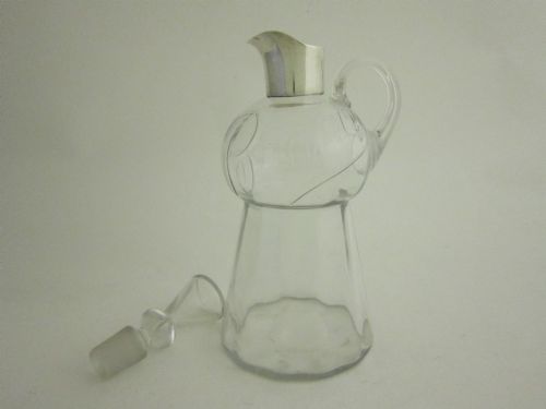 fig 1. Clear glass brandy decanter with a sterling silver collar spout, a single side loop handle, and a geometric glass stopper.